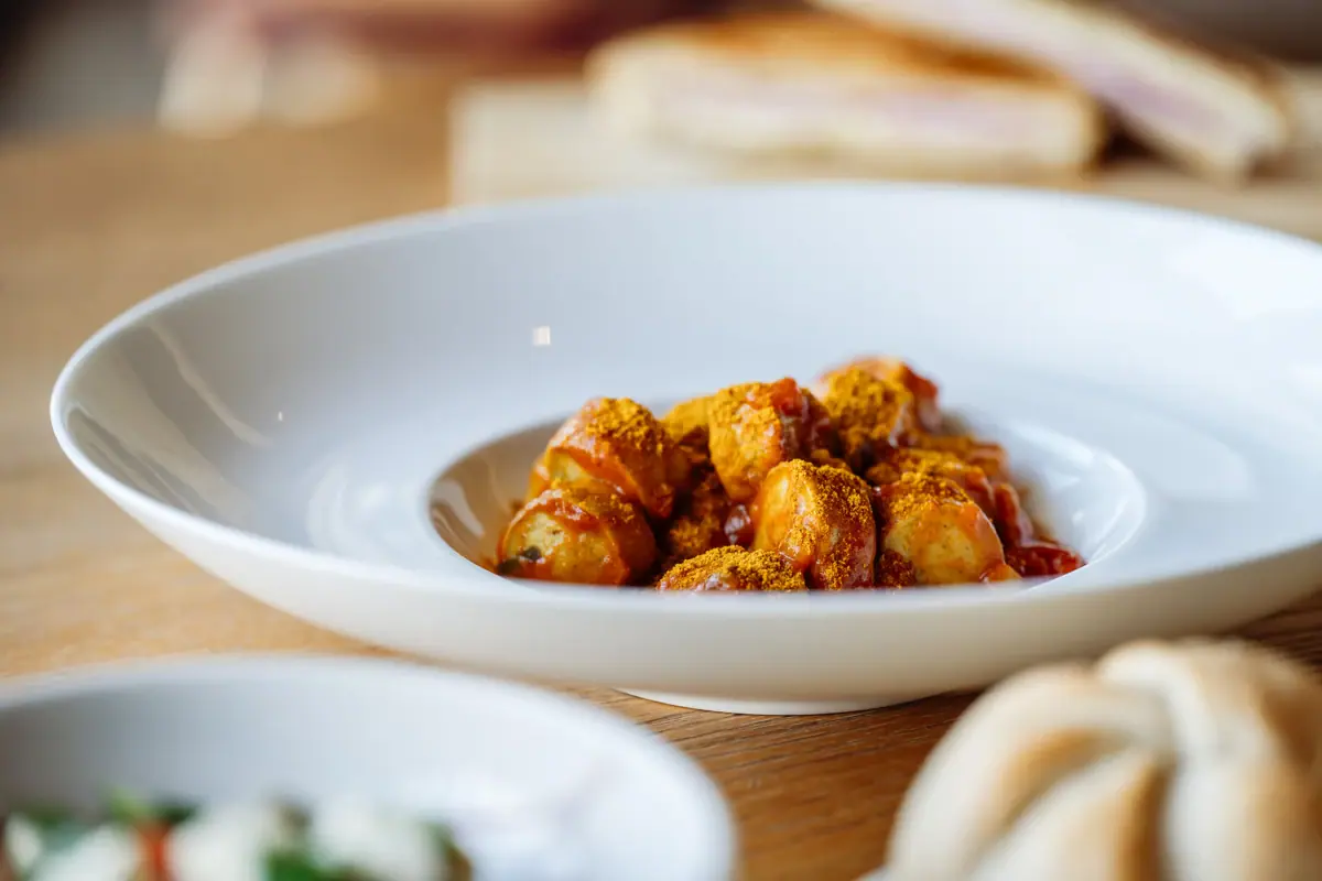 Ein Teller mit Currywurst auf einem Tisch im Bistro des Badehauses Werfenweng..