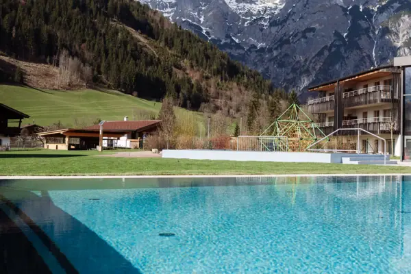 Schwimmbecken mit Gebäude im Hintergrund und Bergen im Hintergrund.